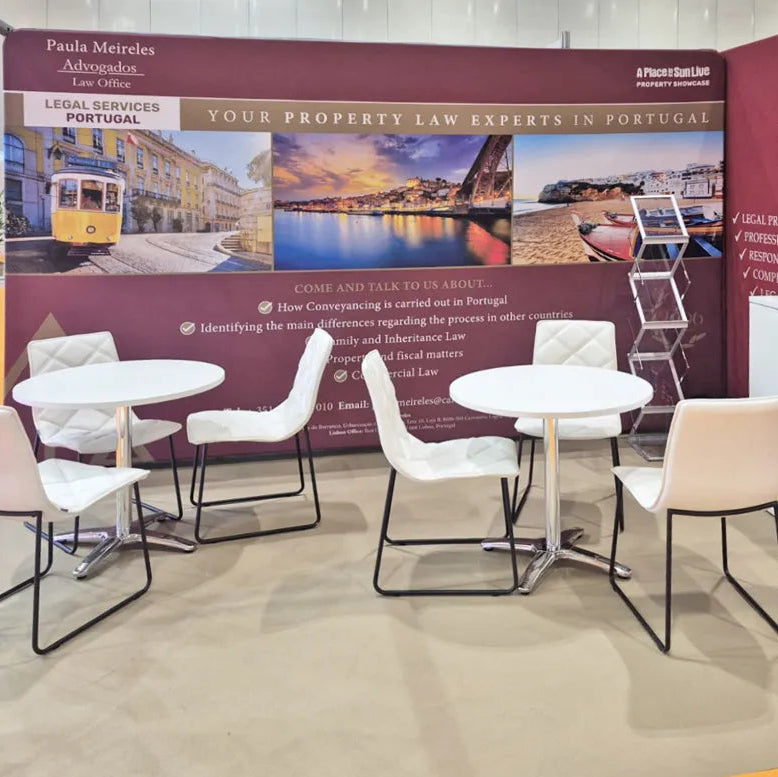 A property law office exhibition booth with a large maroon informational wall, white tables, and several white and blush chairs. Visible text includes 'Paula Meire & Associados' and 'Legal Services Portugal'.