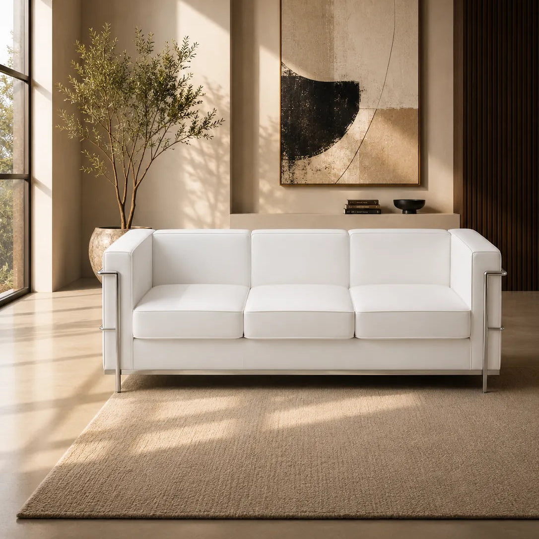 Image of A modern white three-seat sofa in a minimalist, warm-toned living room with a beige rug, a potted plant, and abstract wall art.
