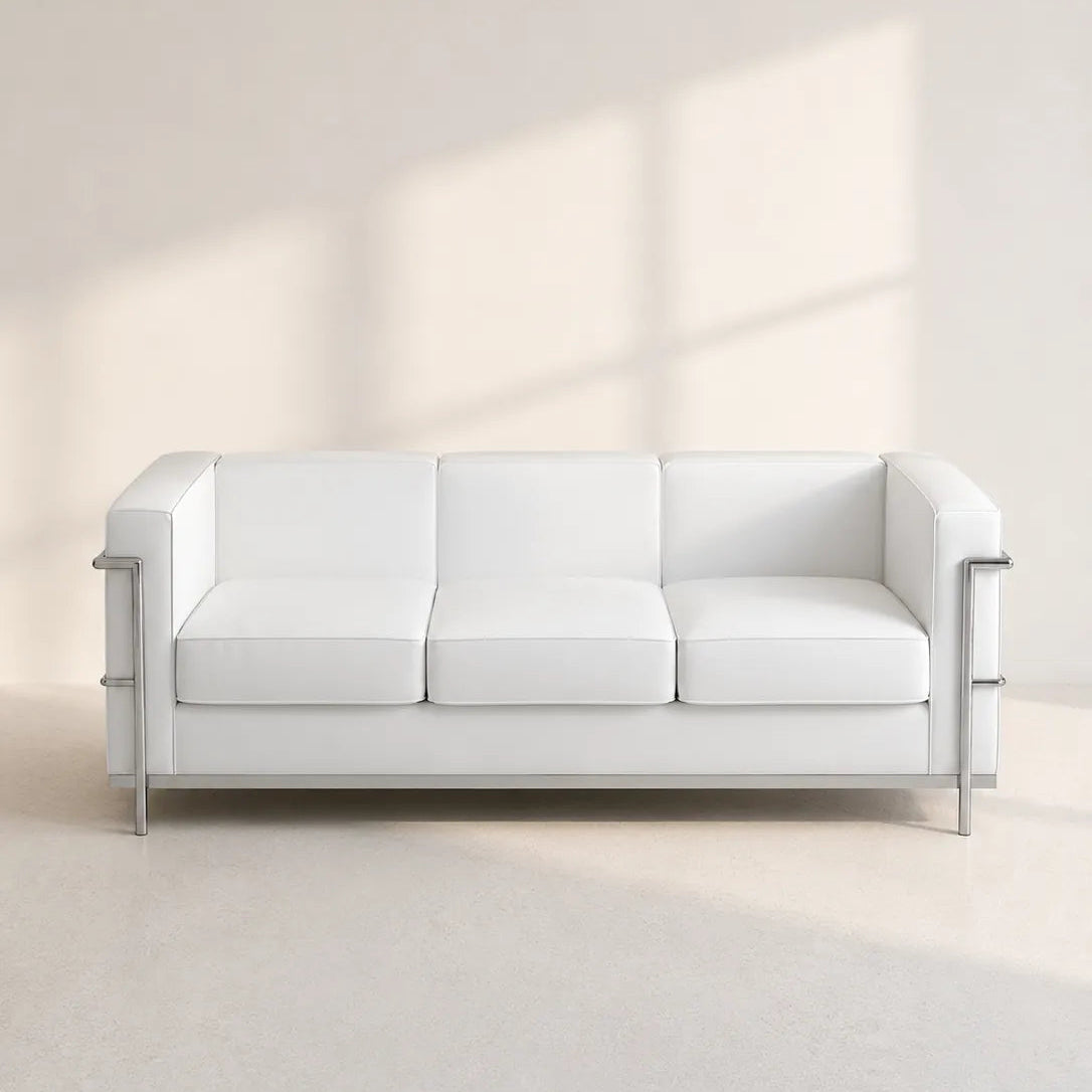 Image of A modern white leather three-seat sofa with slim silver metal legs and side accents, set against a minimalist beige wall with soft window shadow projections.