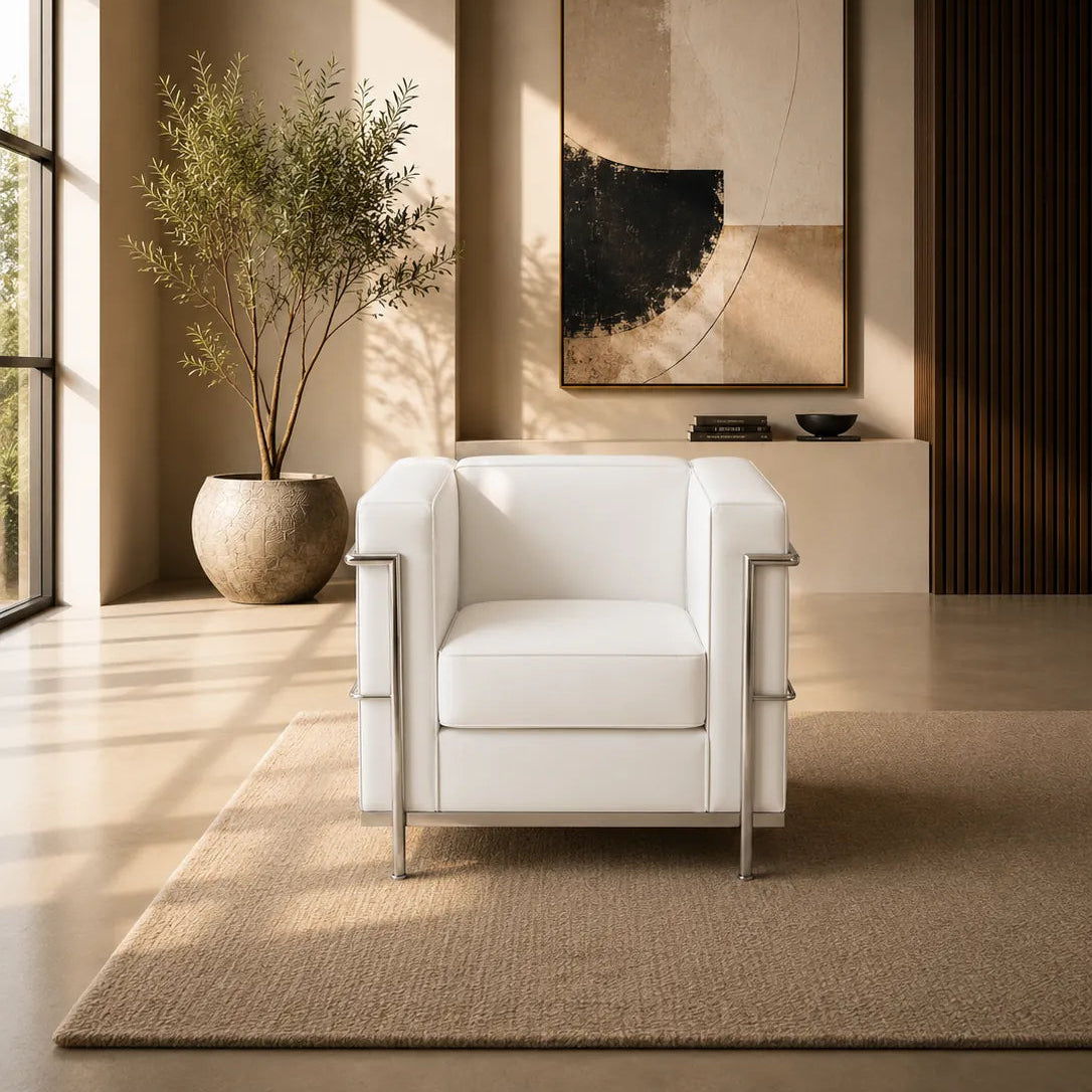 A modern white leather armchair with polished steel side rails and legs, positioned in a minimalist room with warm sunlight casting windowpane shadows on the beige wall and floor.