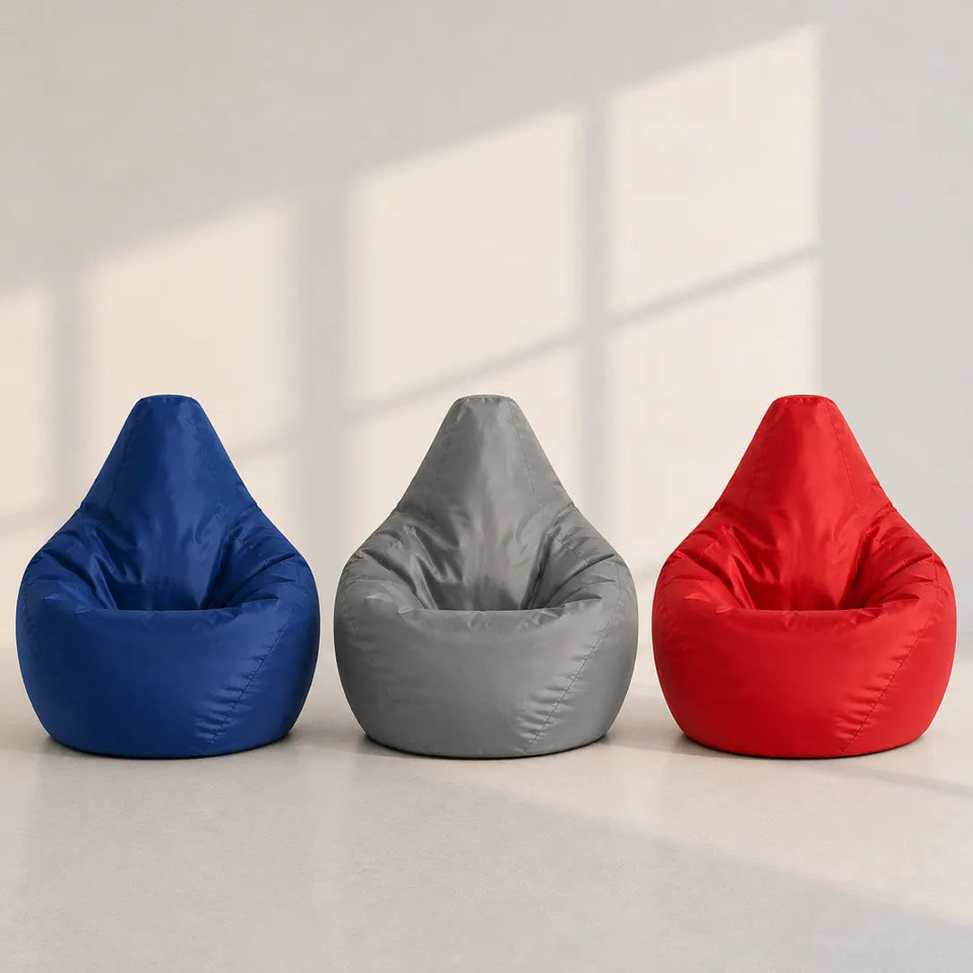 Image of Three teardrop-shaped bean bag chairs in blue, gray, and red, lined up side-by-side on a light gray floor against a beige wall with soft window shadows.