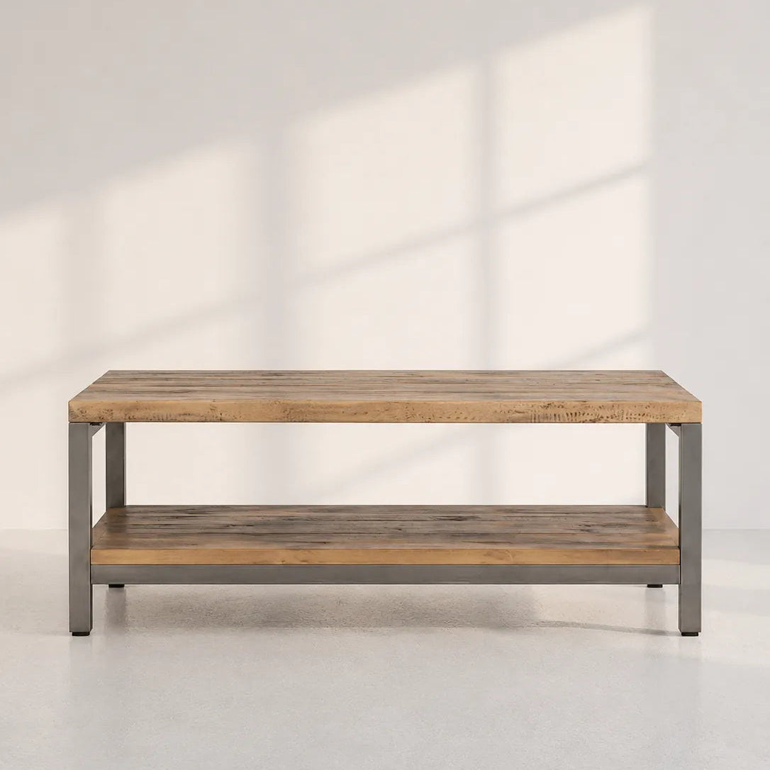 Image of A rectangular coffee table with a rustic light brown wood top and lower shelf, supported by a gray metal frame, set against a light gray wall with soft window shadow patterns.
