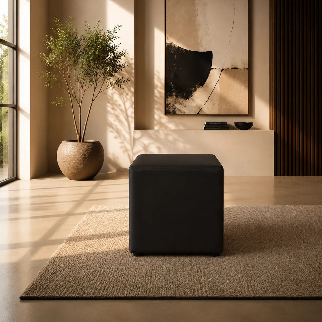 Image of A modern minimalist interior scene featuring a black cube ottoman centered on a textured beige rug, with a large abstract wall art piece and a potted plant in the background.