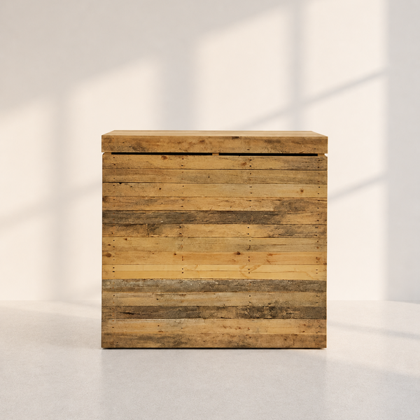 A rustic wooden storage box with a lid, constructed from horizontal reclaimed wood planks in natural brown and beige tones, set against a minimalist off-white wall with soft window shadow patterns.