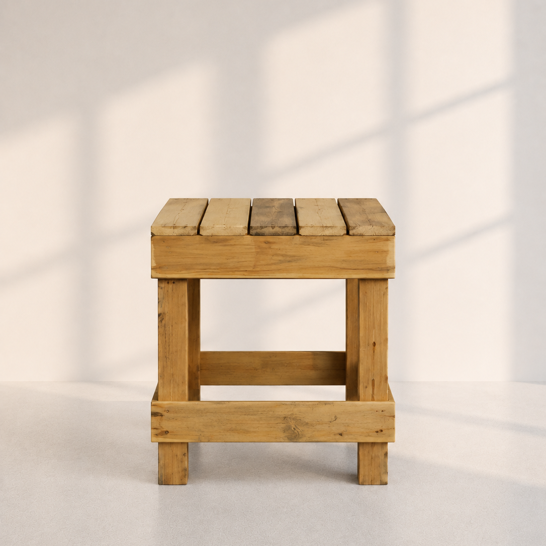 Image of A rustic wooden stool with a slatted top and open side panels, shown against a light neutral wall with soft window-shadow lighting.