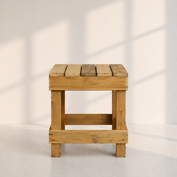 A rustic wooden stool with a slatted top and open side panels, shown against a light neutral wall with soft window-shadow lighting.