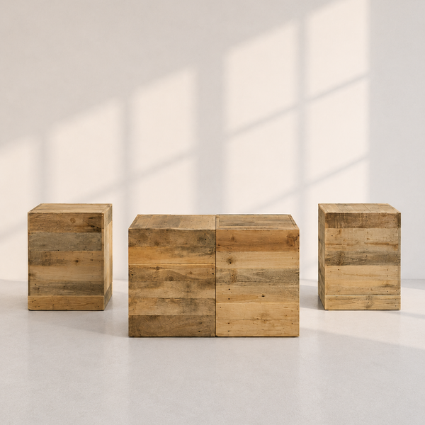 Three rustic wooden storage boxes or crates in varying sizes, arranged on a light gray floor against a white wall with soft window shadow projections.