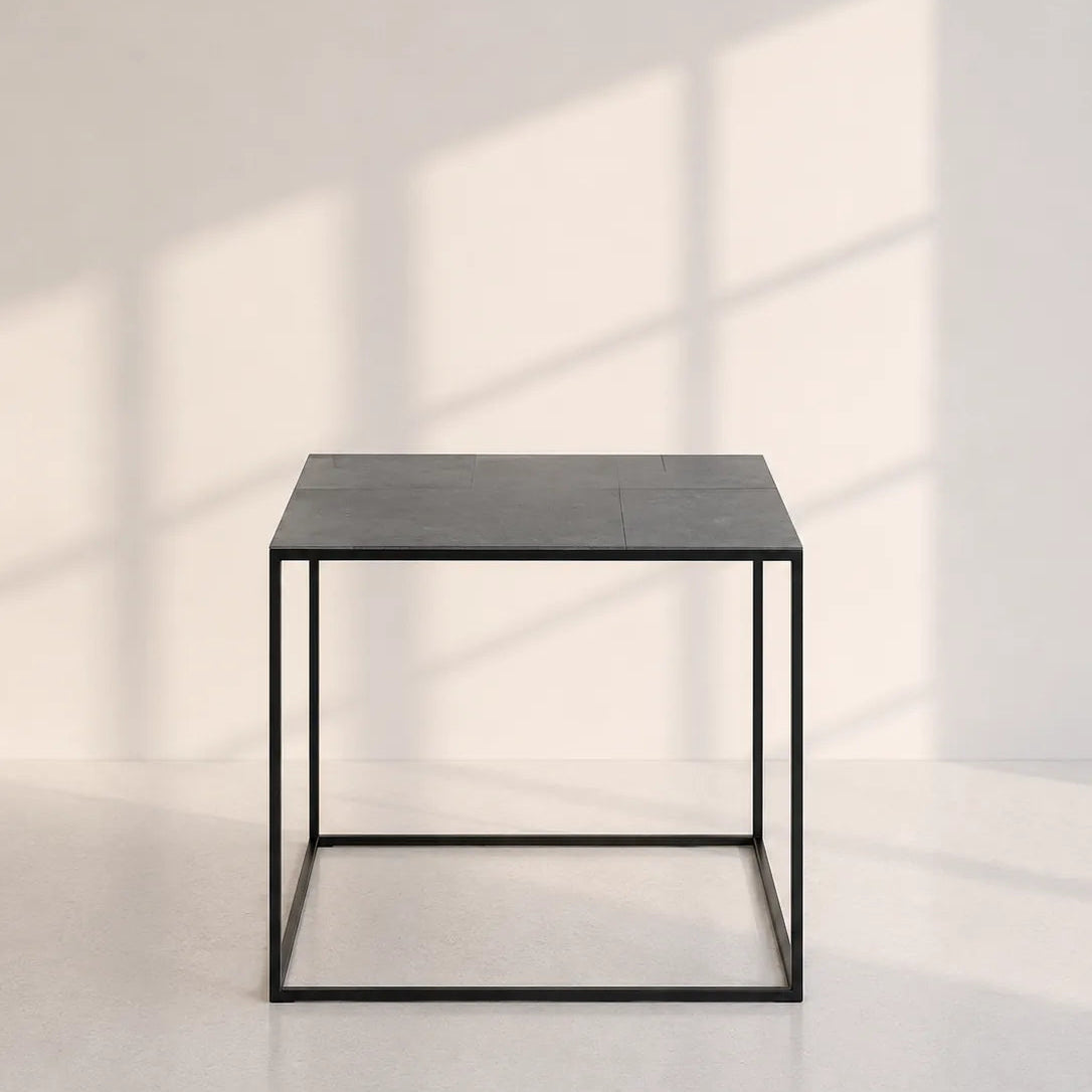 Image of A modern square side table with a dark gray wood top and a black metal frame, set against a minimalist off-white wall with soft window shadow patterns.