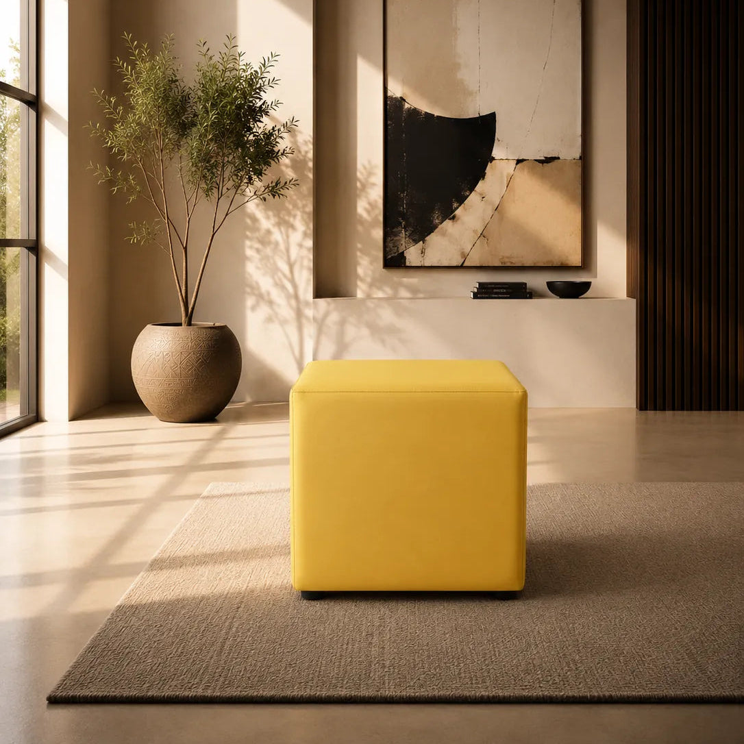 Image of A modern yellow cube ottoman sits on a textured gray rug in a minimalist, warm-toned living room with a large abstract wall art piece and a potted plant in the background.