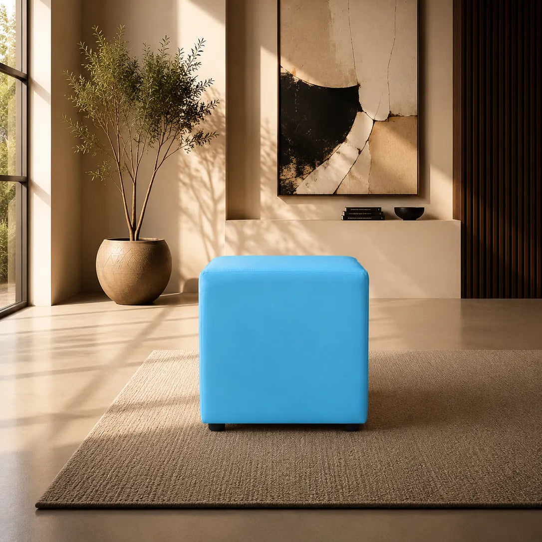 Image of A bright blue cube ottoman or stool placed on a textured beige rug in a modern, sunlit interior room with a potted plant, wall art, and warm ambient lighting.