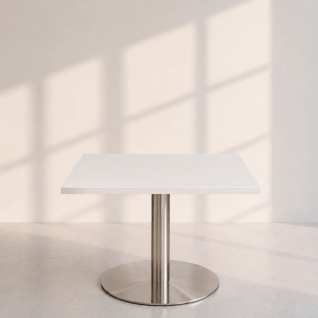Image of A modern square dining table with a white top and a brushed stainless steel pedestal base, set against a minimalist light gray wall with soft window shadow patterns.