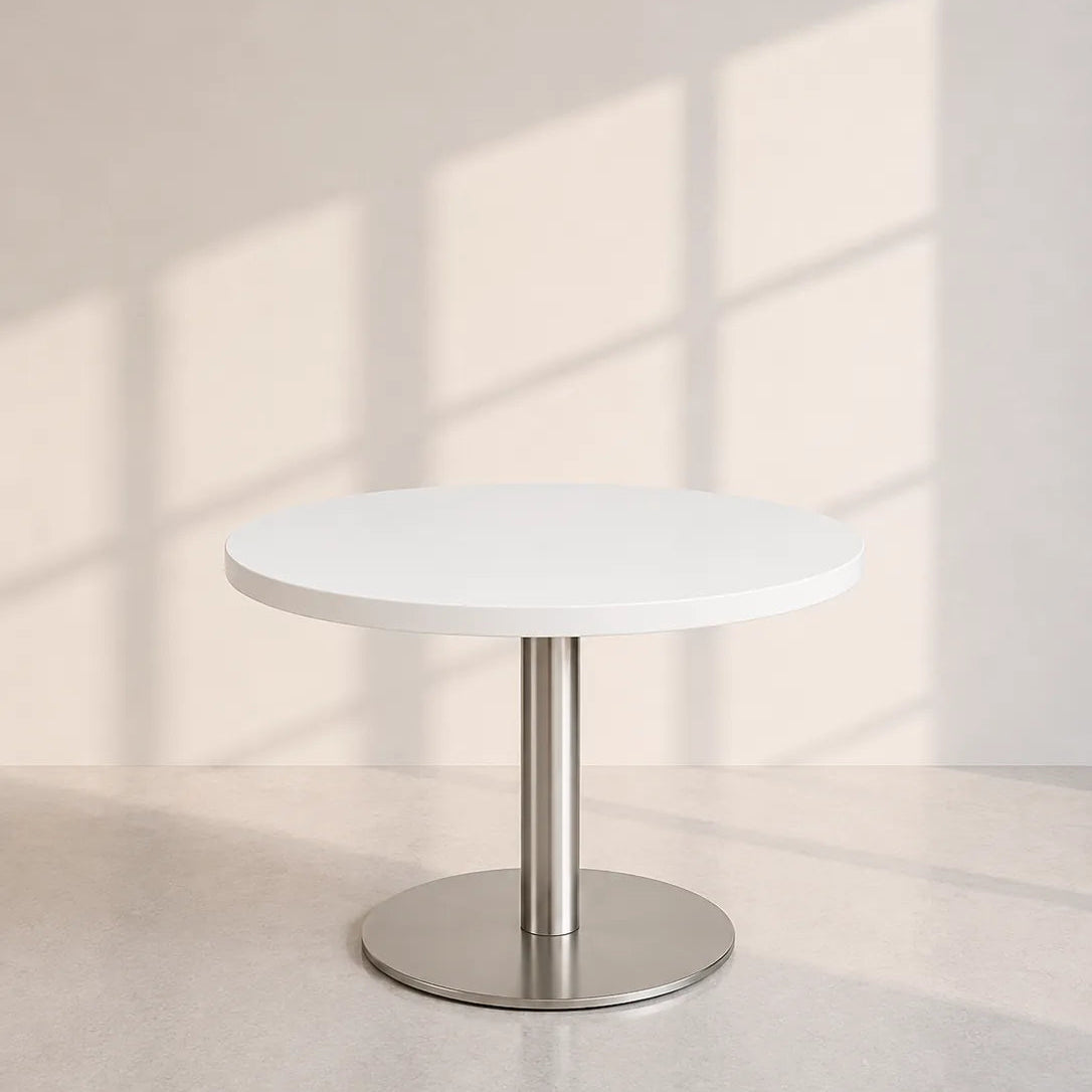 Image of A minimalist round white table with a brushed silver metal pedestal base, set against a warm beige wall with soft window shadow patterns.