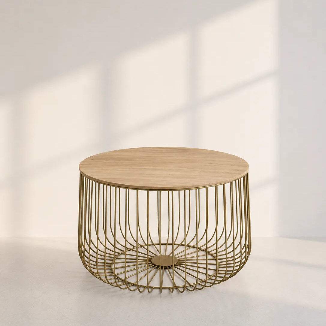 Image of A modern round side table with a light natural wood top and a gold-toned wireframe cylindrical base, set against a minimalist off-white wall with soft window shadow projections.
