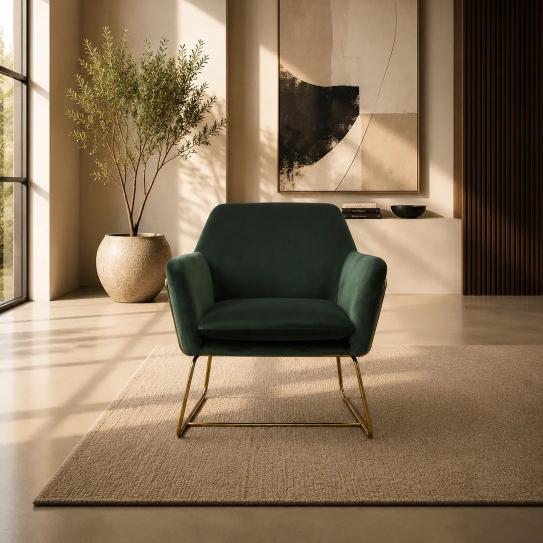 Image of A modern dark green velvet armchair with gold metal legs is placed on a beige rug in a sunlit minimalist living room. A large abstract art print hangs on the wall behind it, with a potted plant to the left and warm ambient lighting casting shadows across the floor.