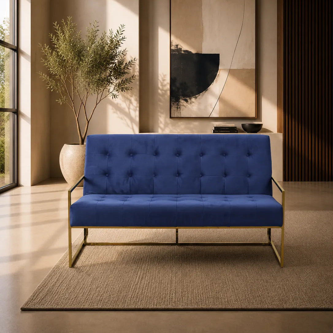 Image of A modern two-seater loveseat sofa with deep blue tufted upholstery and a slim gold metal frame, positioned in a stylishly decorated living room with a beige rug, wall art, and a potted plant.