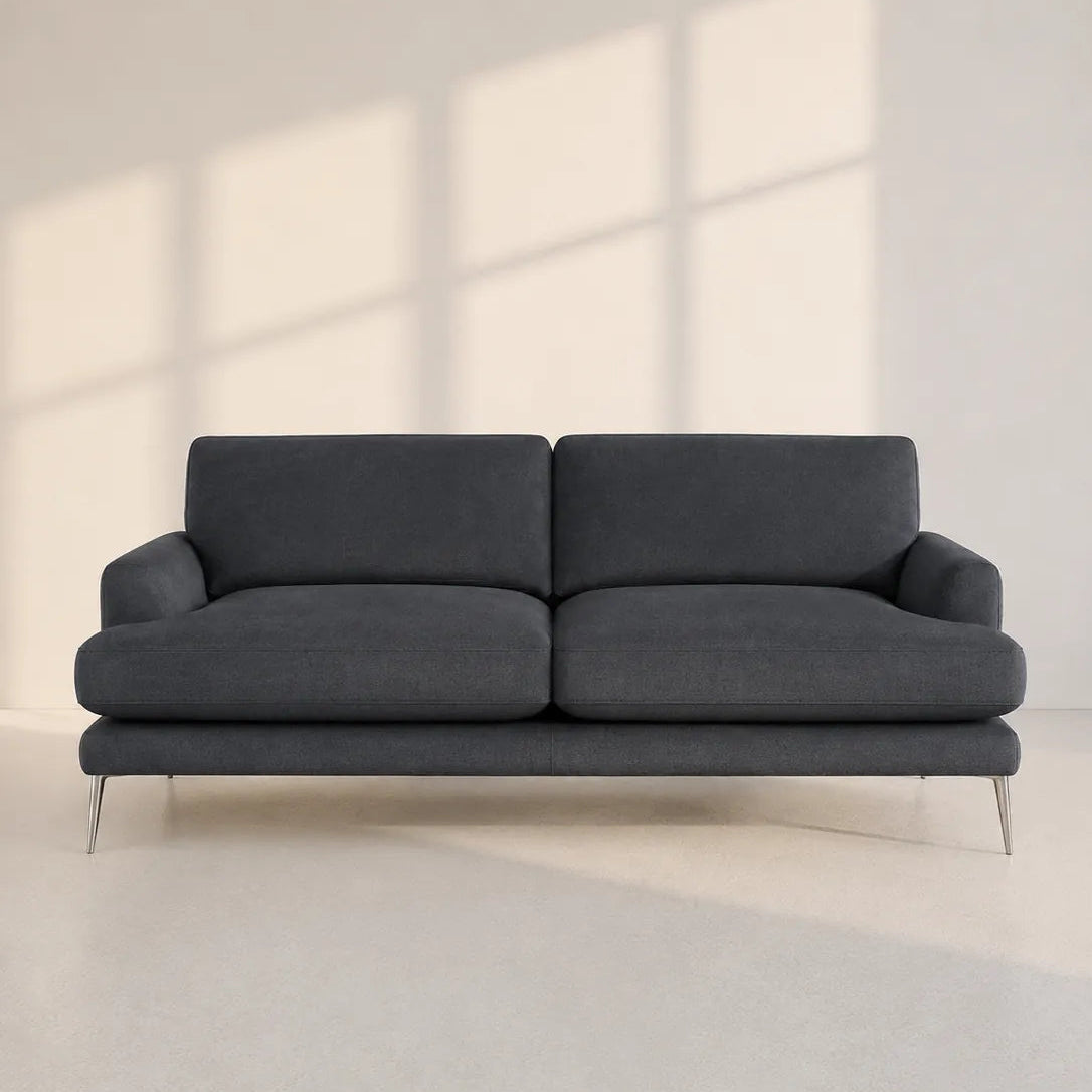 Image of A modern two-seater sofa in dark charcoal gray fabric, supported by slim metal legs, set against a minimalist off-white wall with soft window shadow patterns.