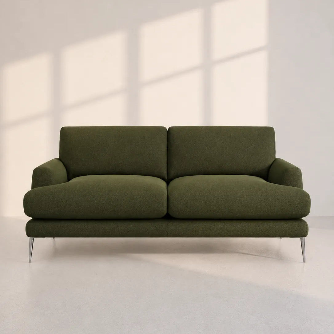 Image of An olive green two-seater sofa with slim metallic legs, positioned against a minimalist off-white wall with soft window-pane shadows cast across it.