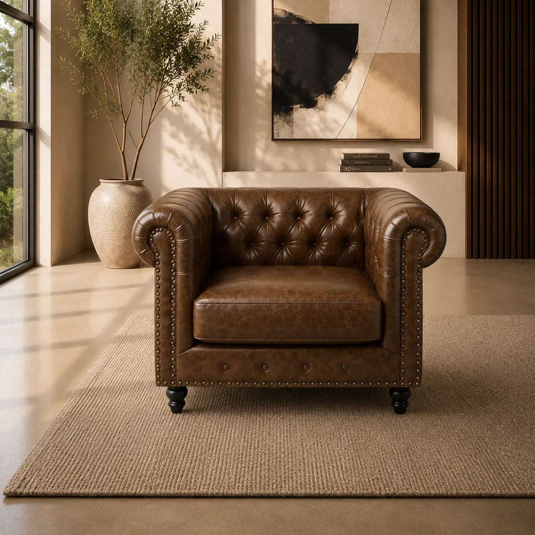 Image of A brown leather tufted armchair with nailhead trim is placed in a styled interior room with a rug, potted plant, wall art, and warm ambient lighting.