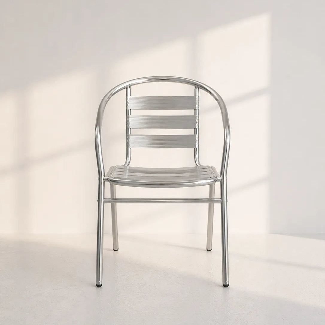 A modern metal chair with a curved backrest and horizontal slats, shown in a minimalist studio setting with soft window-box shadows on a white wall and floor.