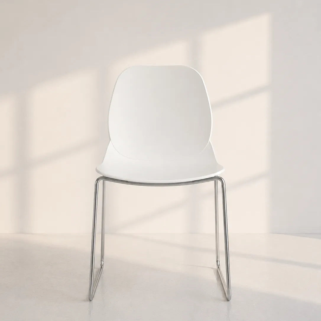 Image of A modern white plastic chair with a thin silver metal frame, set against a minimalist white wall and floor with soft window shadow patterns.