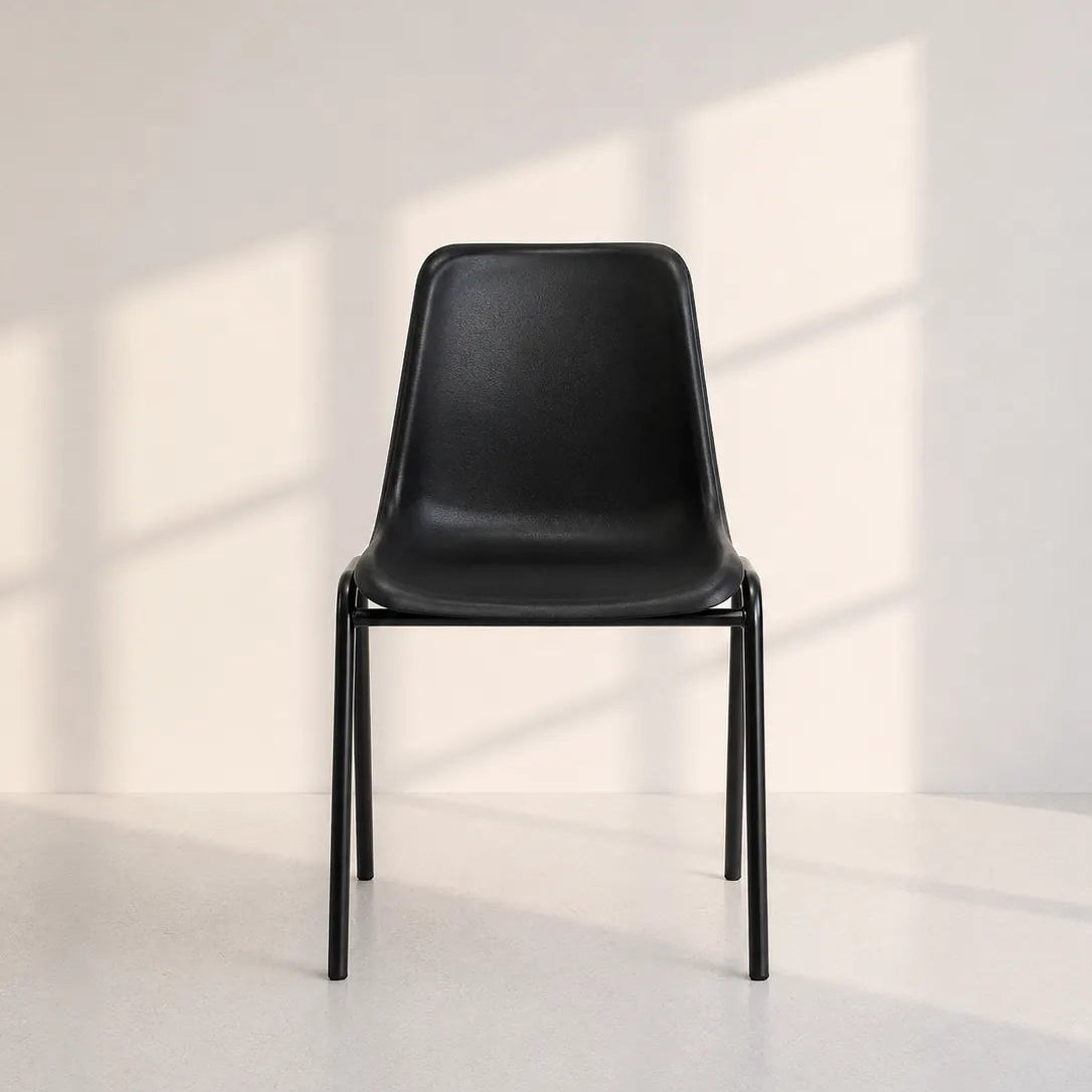 Image of A modern black molded plastic dining chair with a slim metal frame, positioned against a minimalist off-white wall with soft window shadow patterns.