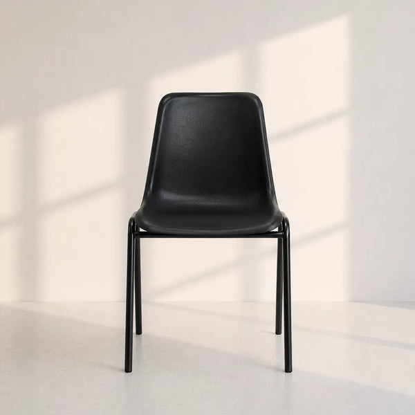 A modern black molded plastic dining chair with a slim metal frame, positioned against a minimalist off-white wall with soft window shadow patterns.