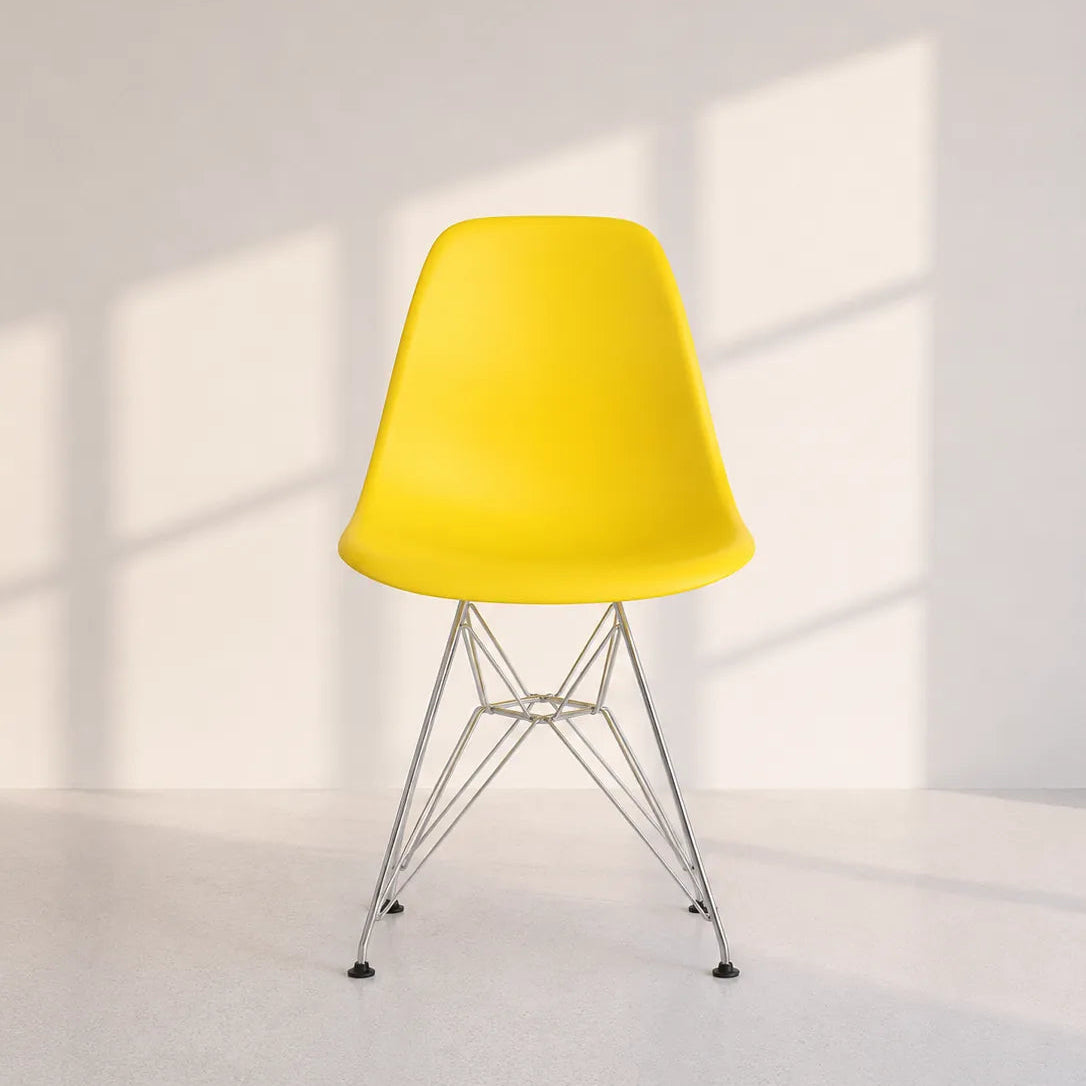 Image of A modern yellow molded plastic side chair with a chrome wire Eames-style base, set against a minimalist white wall with soft window shadow patterns.