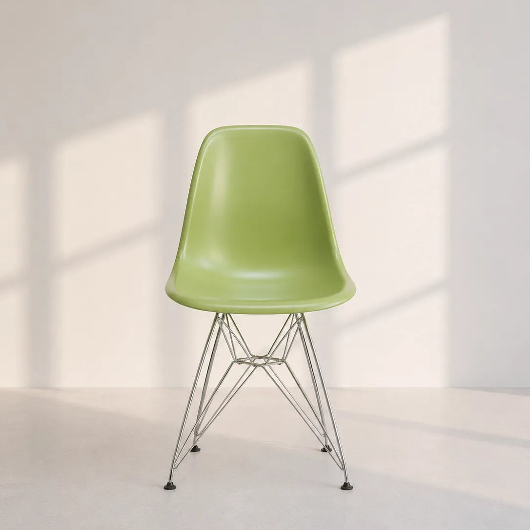 A light green molded plastic side chair with a chrome wire pedestal base, set against a minimalist off-white wall with soft window shadow patterns.