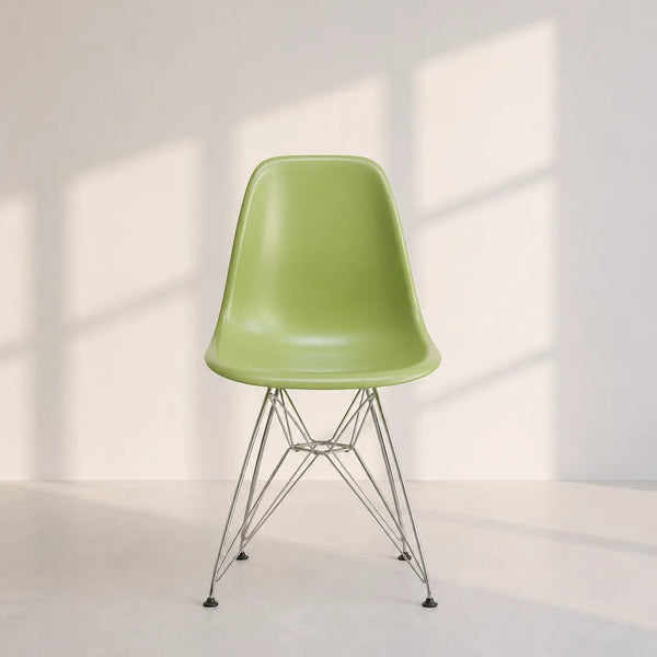 A light green molded plastic side chair with a chrome wire pedestal base, set against a minimalist off-white wall with soft window shadow patterns.