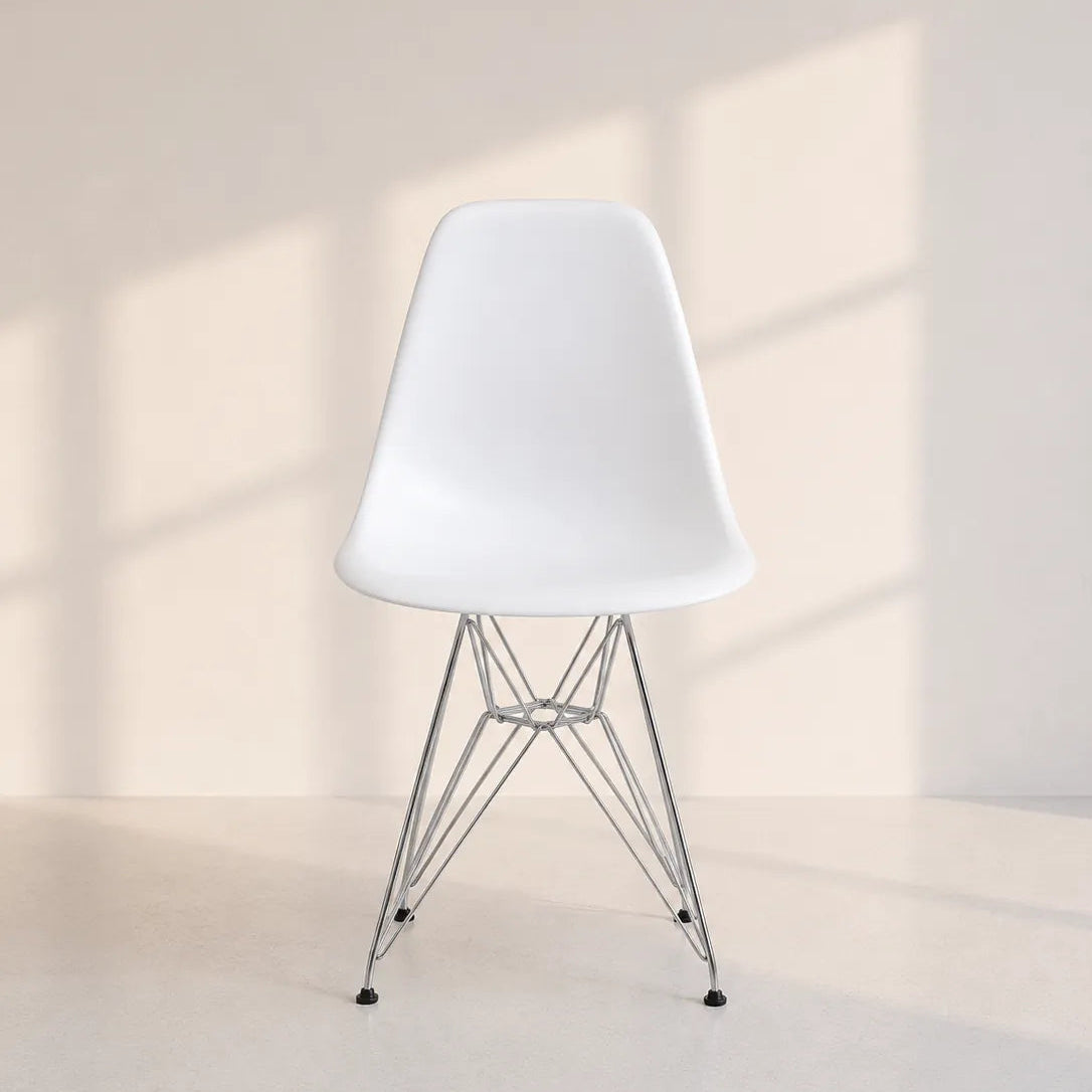 Image of A modern white molded plastic side chair with a chrome wire metal base, set against a minimalist beige wall with soft window shadow patterns.