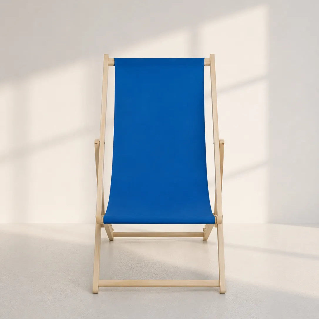 A classic wooden deck chair with a vibrant blue canvas sling seat and backrest, set against a minimalist white wall with soft window shadows.
