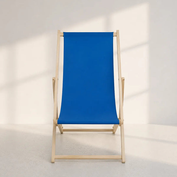 A classic wooden deck chair with a vibrant blue canvas sling seat and backrest, set against a minimalist white wall with soft window shadows.