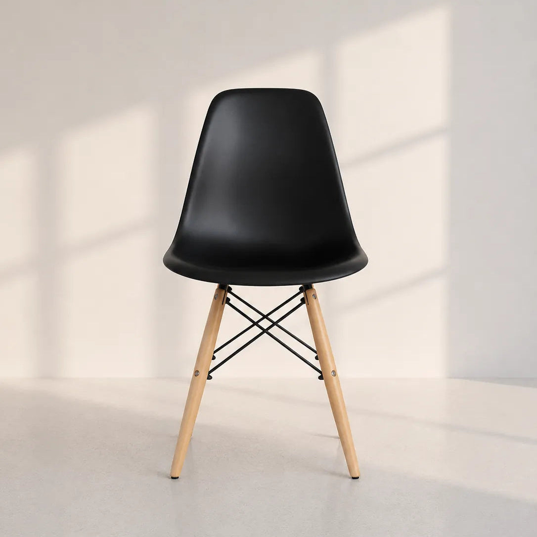 Image of A modern black molded plastic side chair with light natural wood legs and black metal crisscross support rods, set against a minimalist off-white wall with soft window shadow patterns.