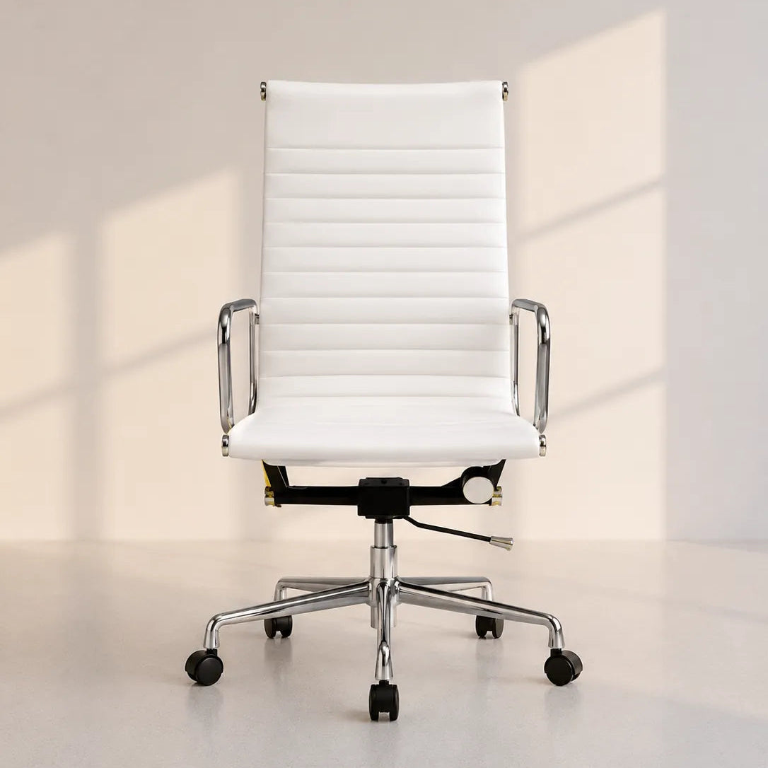 A modern white faux-leather office chair with a high ribbed backrest, chrome metal armrests and base, and black casters, shown in a minimalist studio setting with soft window-box shadows.