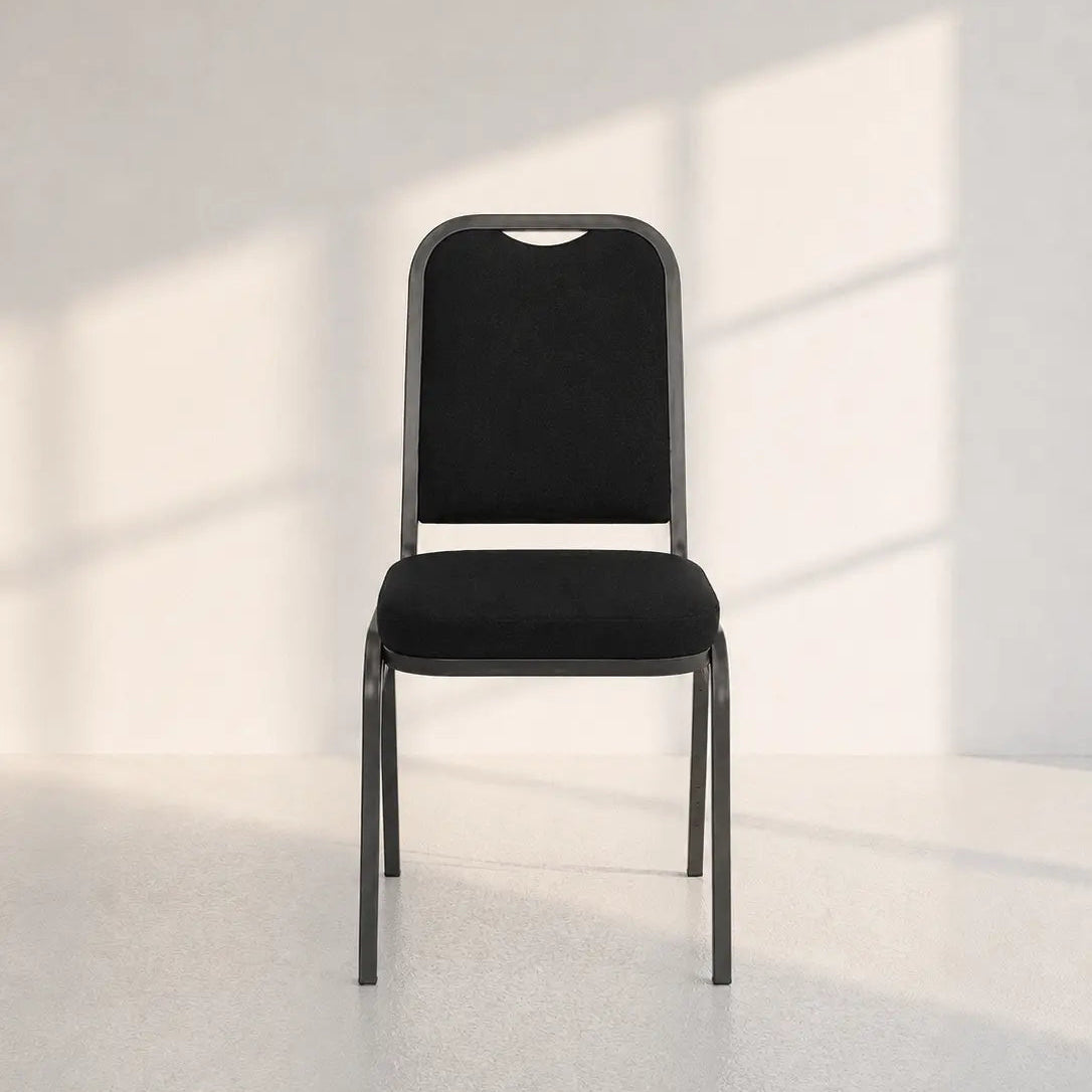 Image of A modern black fabric-upholstered chair with a dark metal frame, positioned centrally in a minimalist white room with soft window shadow patterns on the wall.