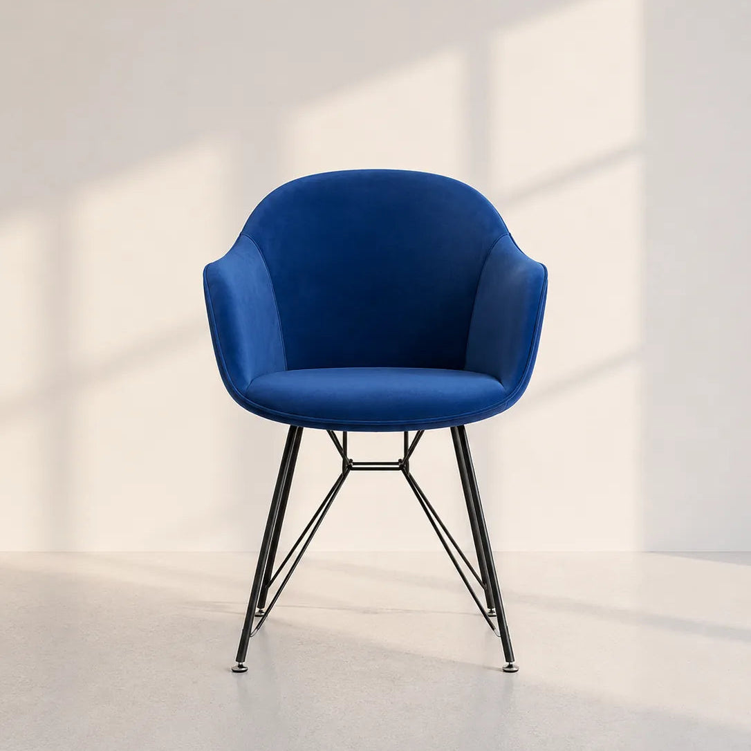 A modern blue upholstered armchair with a curved backrest and slim black metal legs, set against a minimalist off-white wall with soft window-box shadows.