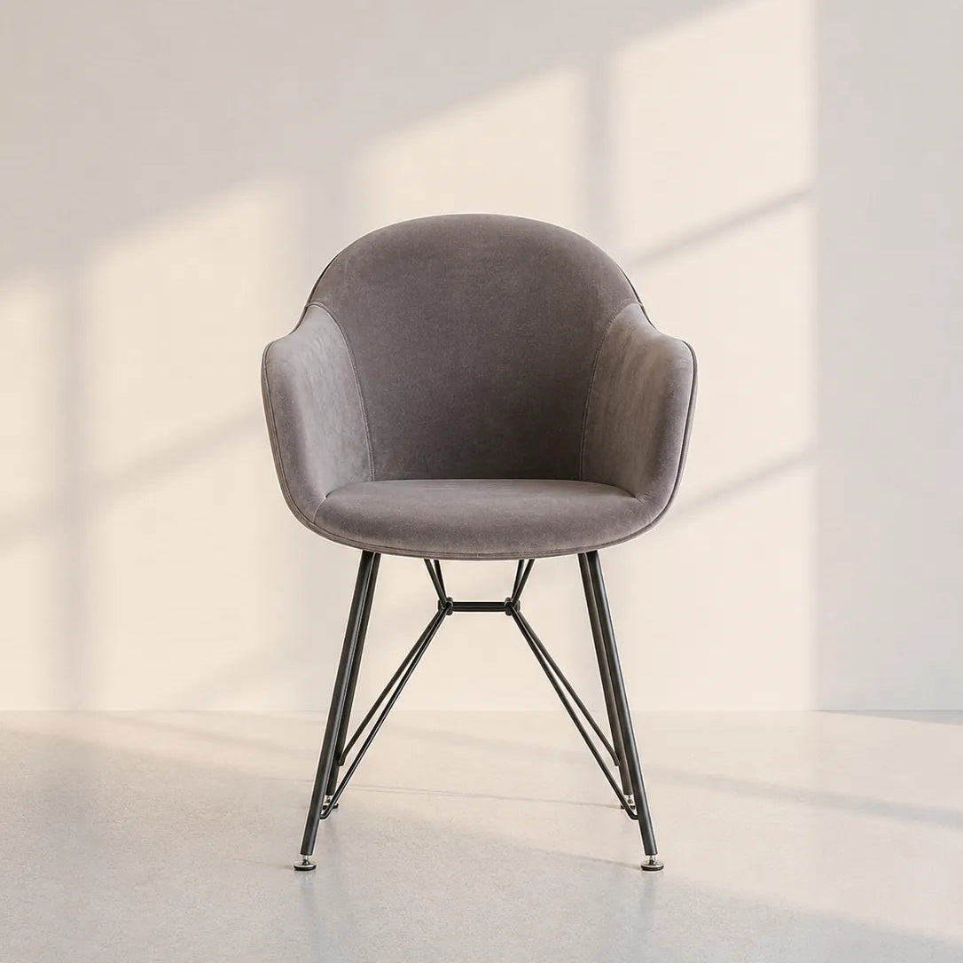 Image of A modern upholstered accent chair with a curved gray fabric seat and backrest, supported by slim black metal legs, set against a minimalist off-white wall with soft window shadow patterns.