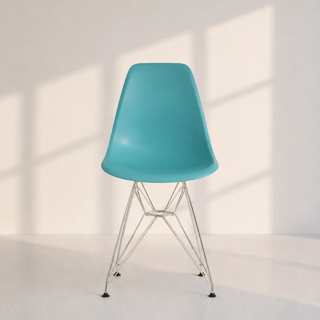 A modern molded plastic side chair with a turquoise blue seat and chrome wire legs, set against a minimalist off-white wall with soft window shadow patterns.