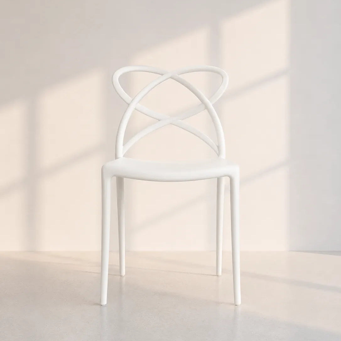 A modern white molded chair with a curved, looped backrest, shown in a minimalist room with soft window-box shadows cast on a light beige wall and floor.