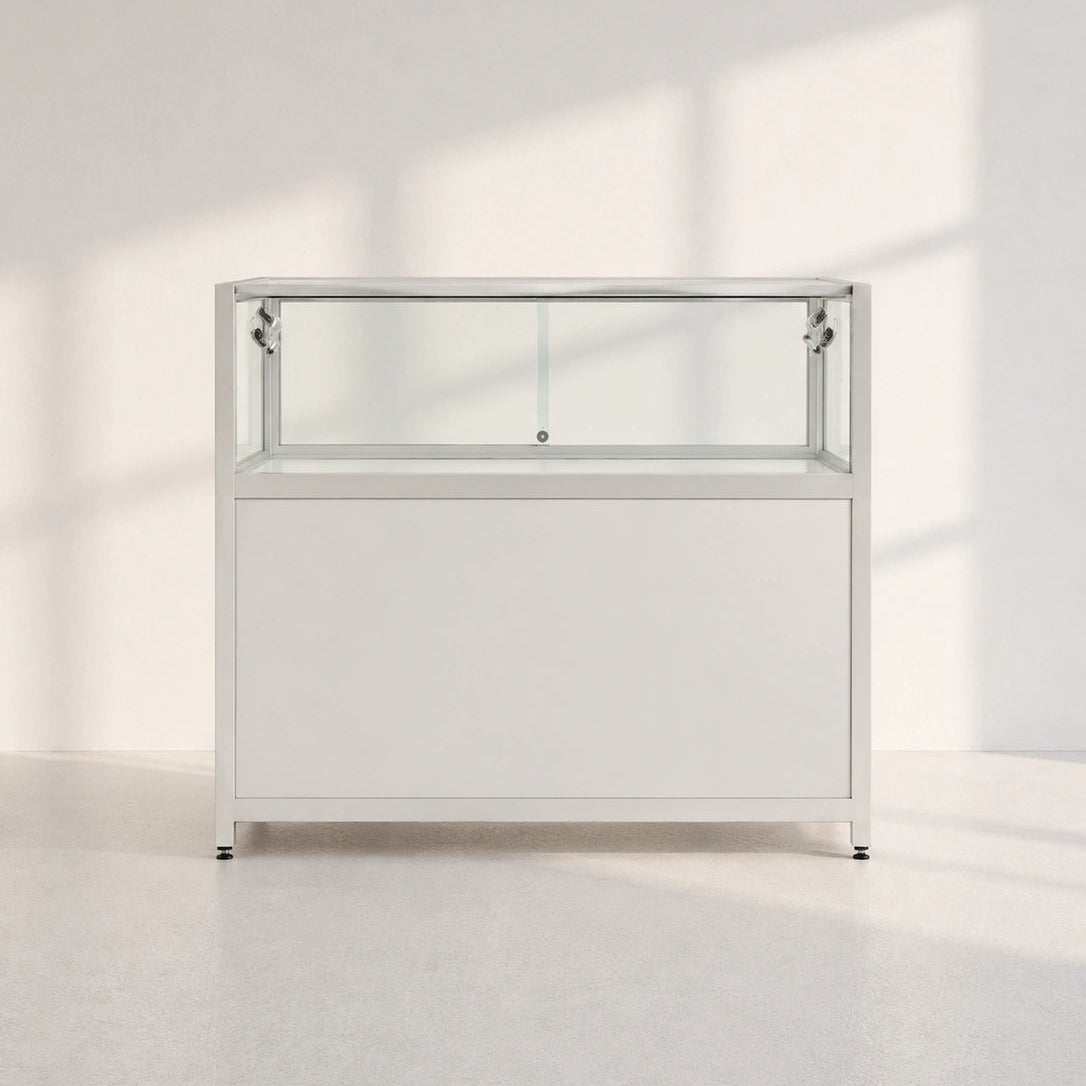 Image of A modern white display cabinet with a glass top shelf and a lower door, set against a minimalist white wall with soft window shadows.