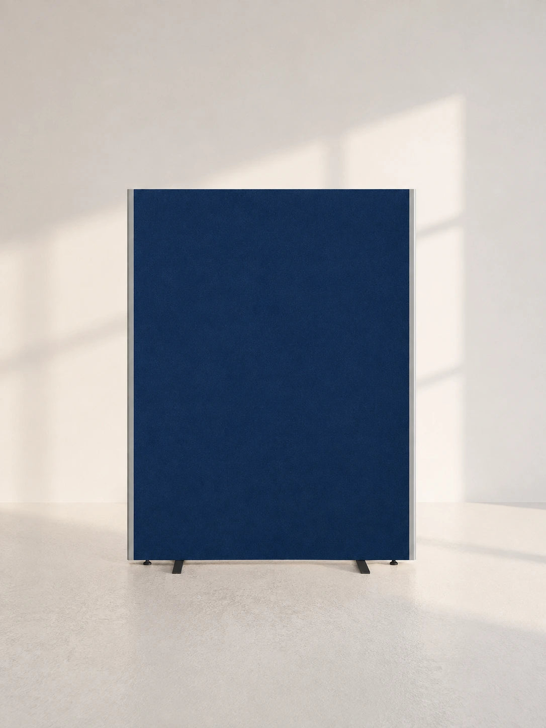 Image of A tall, rectangular navy blue panel or partition with a subtle fabric-like texture, supported by two small black feet, standing on a light concrete floor against a white wall with soft window shadows.