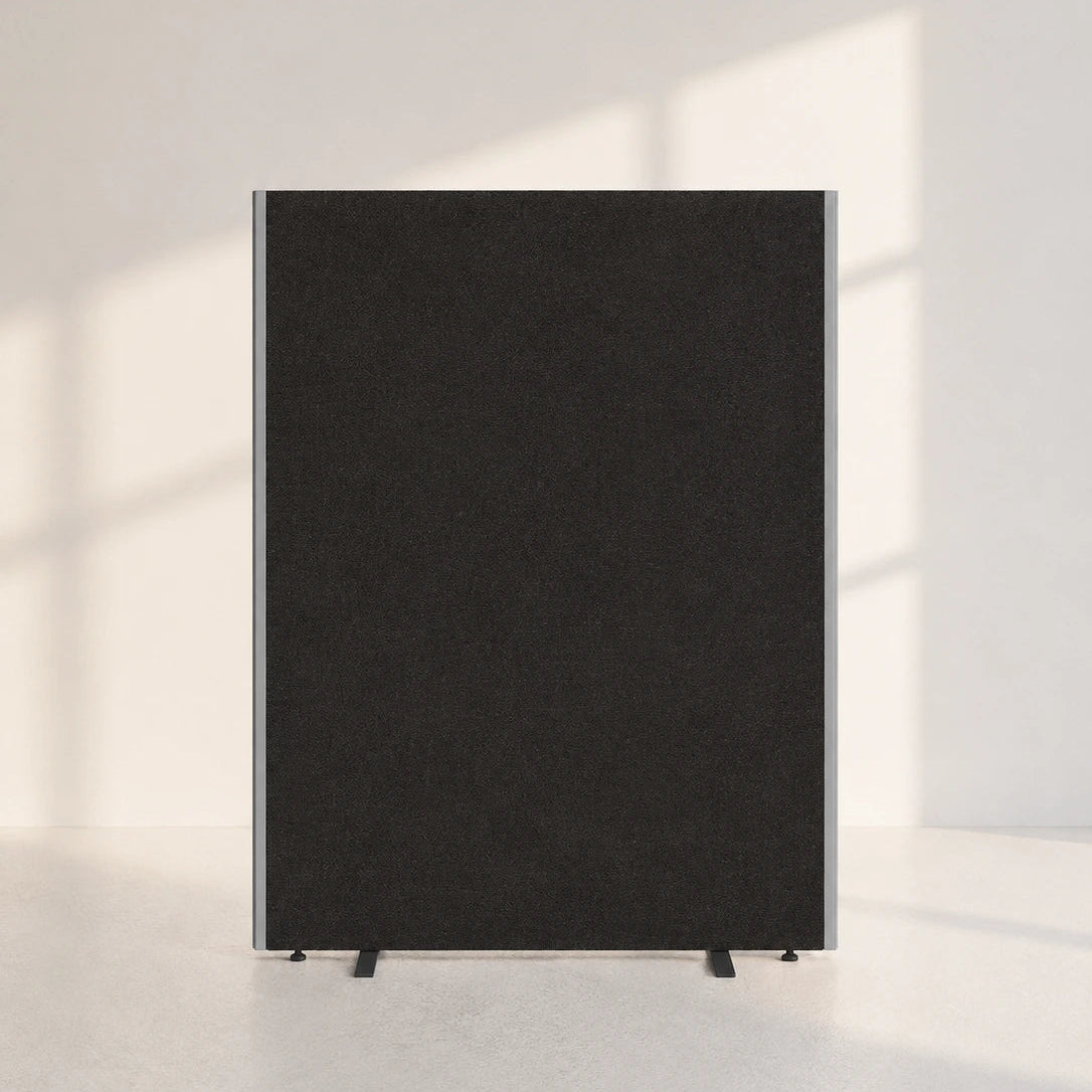 Image of A tall, rectangular black partition panel with a textured fabric surface, supported by two small black feet, set against a minimalist off-white wall with soft window shadow patterns.