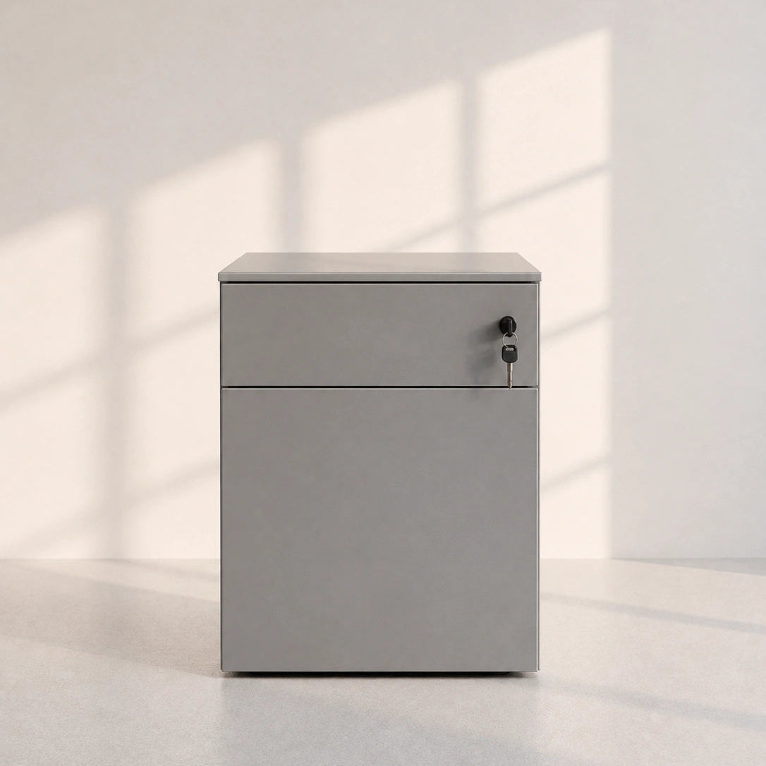 A minimalist light gray metal cabinet with a single drawer and a lower door, featuring a small lock on the right side, set against a light gray wall with soft window shadow patterns.