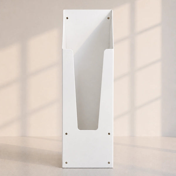 A minimalist white metal wall-mounted document holder with a V-shaped center slot and pre-drilled mounting holes, set against a warm beige wall with soft window shadow patterns.