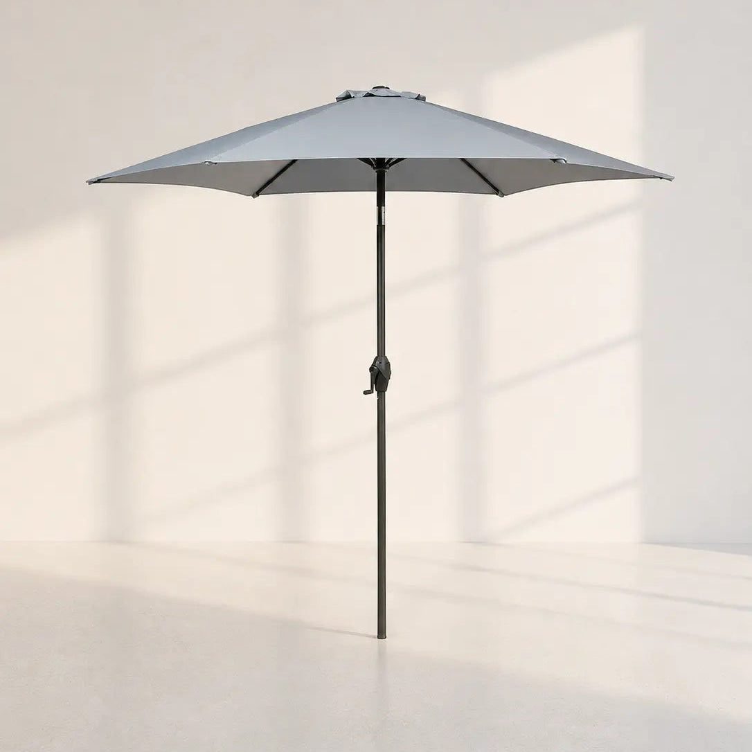 Image of A light gray patio umbrella with a black pole, shown open in a minimalist studio setting with soft window shadow projections on a white wall and floor.