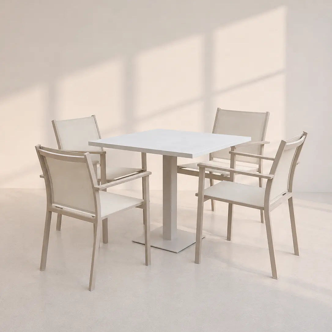 Image of A minimalist dining set featuring a square white table with a central pedestal base and four matching armchairs with light beige woven seats and light wood frames, set against a warm off-white wall with soft window shadow projections.