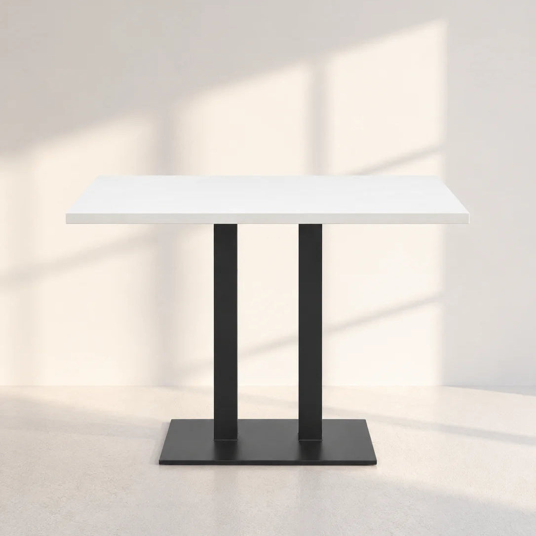 Image of A modern rectangular dining table with a white top and a black double-leg pedestal base, set against a minimalist off-white wall with soft window shadow patterns.