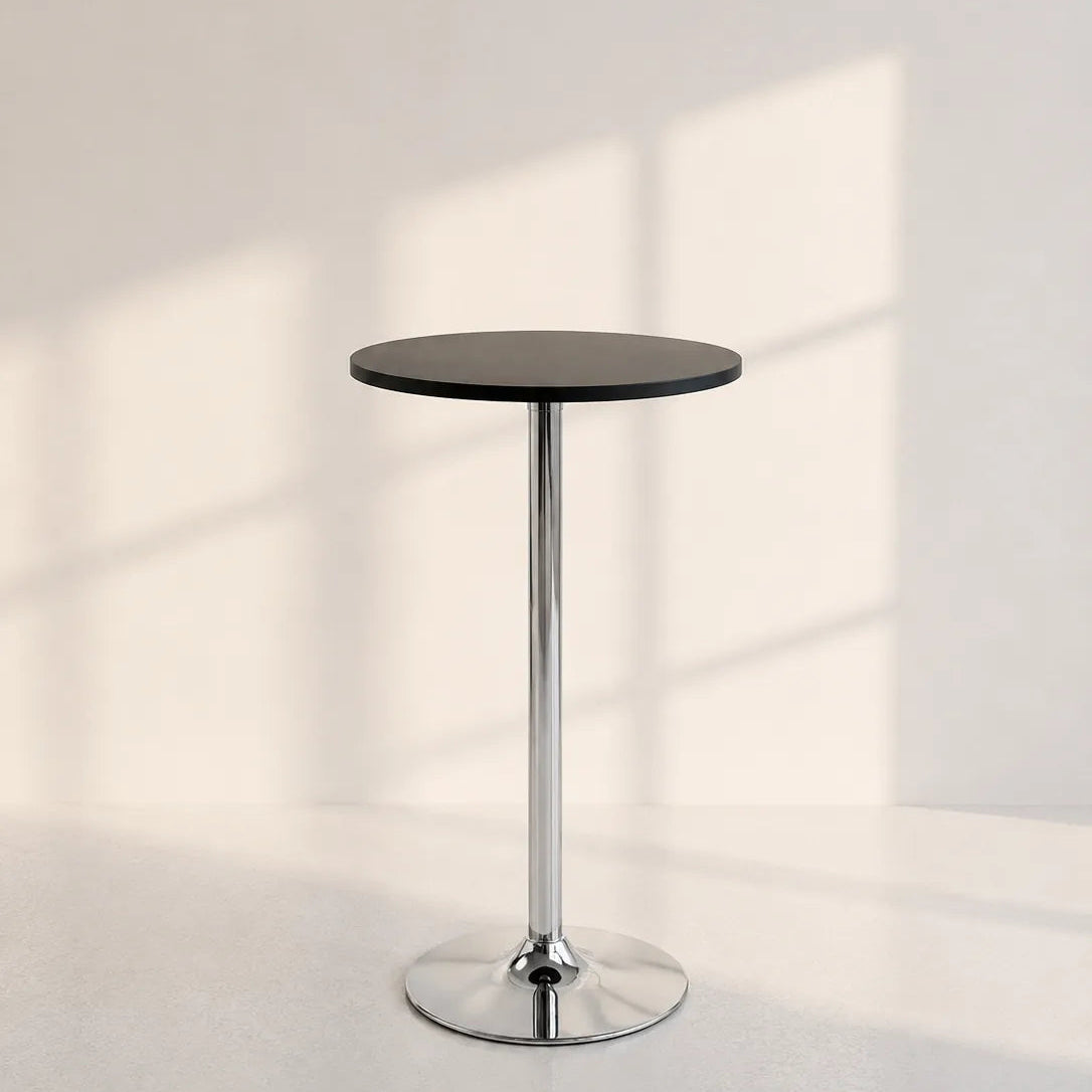 A modern bar-height side table with a round black top and a polished chrome pedestal base, set against a minimalist off-white wall with soft window shadow patterns.