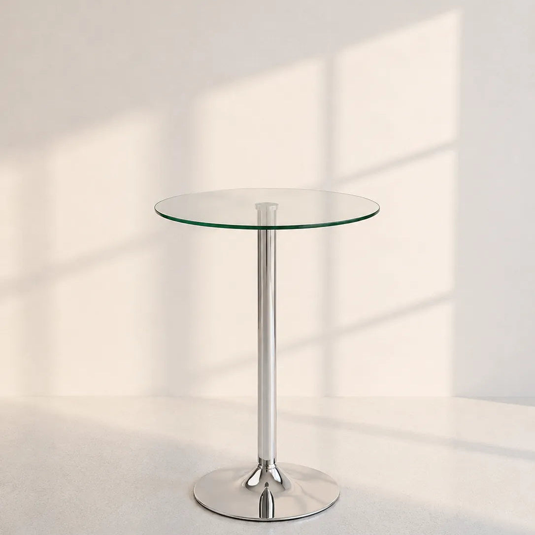 A modern round glass-top side table with a slim polished chrome pedestal base and circular foot, photographed in a bright minimalist room with soft window-shadow lighting.