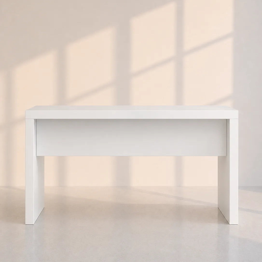 Image of A minimalist white rectangular console table with a thick apron front and block legs, shown in a brightly lit room with soft window shadow patterns on the wall and floor.